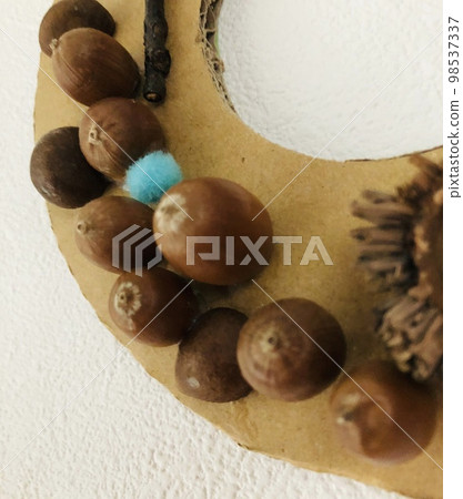 一張紙板花環的照片，上面裝飾著與秋天相關的物品，例如橡子和樹枝。 98537337
