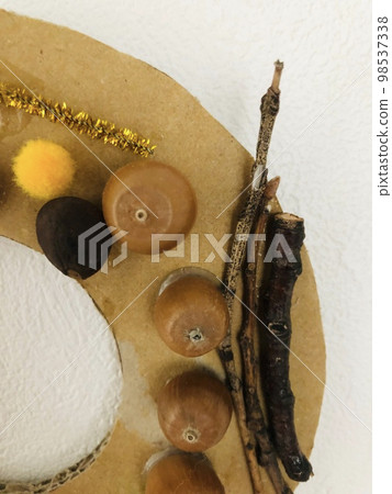 一張紙板花環的照片,上面裝飾著與秋天相關的物品,例如橡子和樹枝。 一張紙板花環的照片,上面裝飾著與秋天相關的物品,例如橡子和樹枝。 98537338