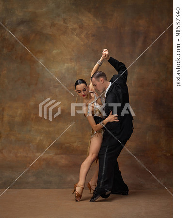 Passionate choreography. Man and woman, professional tango dancers in stylish, beautiful stage costumes performing over dark vintage background Passionate choreography. Man and woman, professional tango dancers in stylish, beautiful stage costumes performing over dark vintage background 98537340