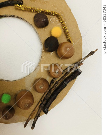一張紙板花環的照片,上面裝飾著與秋天相關的物品,例如橡子和樹枝。 一張紙板花環的照片,上面裝飾著與秋天相關的物品,例如橡子和樹枝。 98537342