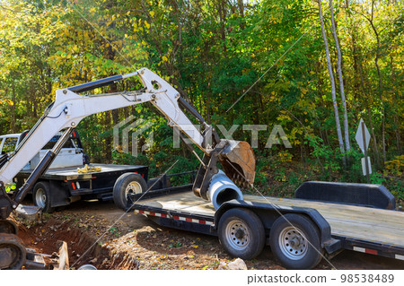 As concrete sewage pipe is being prepared for underground installation worker uses tractor to raise pipe in ground. As concrete sewage pipe is being prepared for underground installation worker uses tractor to raise pipe in ground. 98538489
