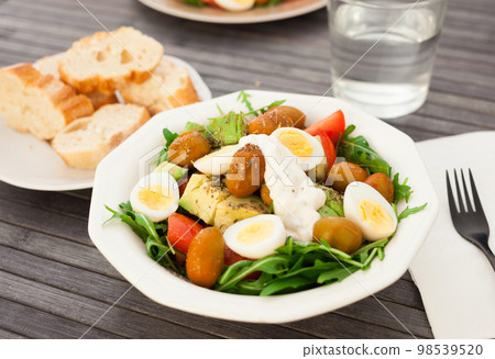 dish of fresh vegetables arugula, avocado, cherry tomatoes with olives and quail eggs on dining table 98539520