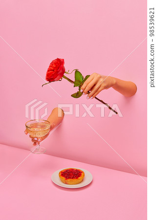Food pop art photography. Female hand sticking out pink paper with champagne and rose flower over delicious berry tart 98539621