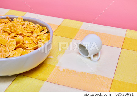 Food pop art photography. Bowl with cereal, corn flakes on yellow tablecloths with milk jar and spilled milk. Breakfast time 98539681
