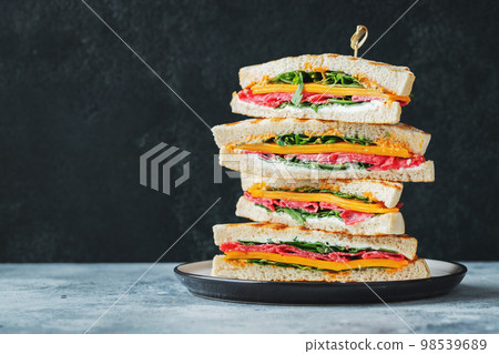 Big homemade sandwich with sausage, cheese and arugula on a dark concrete background 98539689