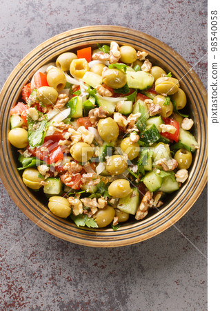 Vegetarian green olives salad with walnuts, tomatoes, cucumbers seasoned with pomegranate molasses close-up in a plate. Vertical top view 98540058