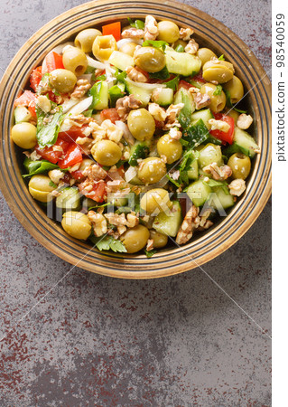 Vegetable vegan diet salad with green olives, walnuts, tomatoes, cucumbers, parsley close-up in a plate. Vertical top view 98540059