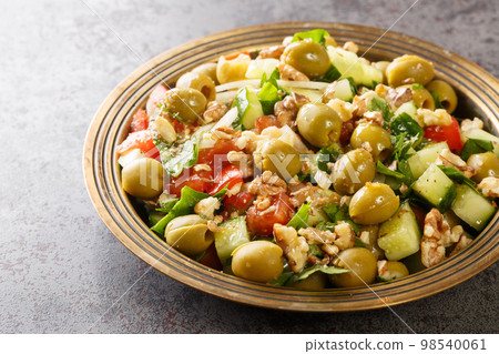Turkish green olives salad with walnuts, tomatoes, cucumbers, parsley close-up in a plate. Horizontal 98540061