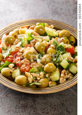 Vegetarian green olives salad with walnuts, tomatoes, cucumbers seasoned with pomegranate molasses close-up in a plate. Vertical Vegetarian green olives salad with walnuts, tomatoes, cucumbers seasoned with pomegranate molasses close-up in a plate. Vertical 98540064