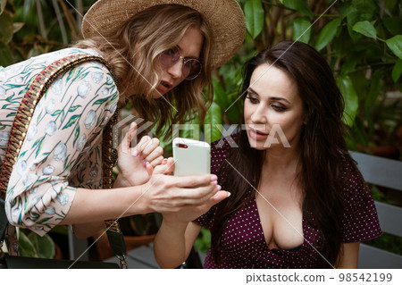 Two girlfriends in the park looking at the phone Two girlfriends in the park looking at the phone 98542199