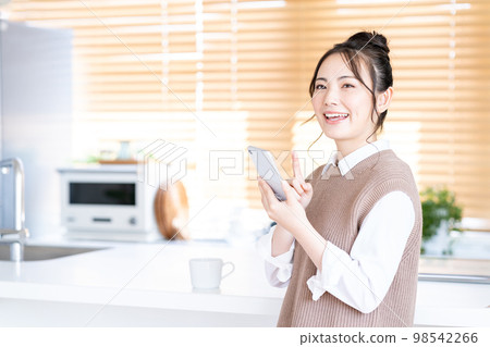 一位年輕女子在廚房裡操作智能手機。 一位年輕女子在廚房裡操作智能手機。 98542266