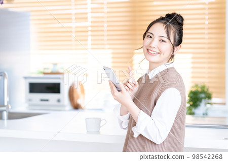 A young woman operating a smartphone in the kitchen. 98542268