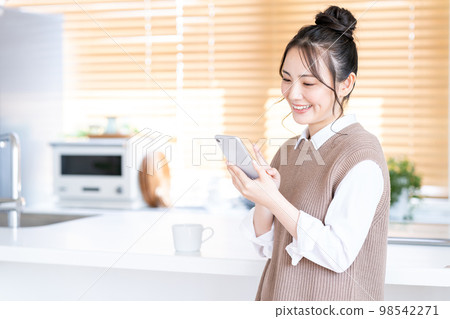 A young woman operating a smartphone in the kitchen. A young woman operating a smartphone in the kitchen. 98542271