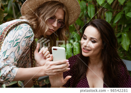 Two girlfriends in the park looking at the phone Two girlfriends in the park looking at the phone 98542281