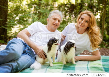 Mature couple in the forest lie on a blanket with a dog Mature couple in the forest lie on a blanket with a dog 98542282