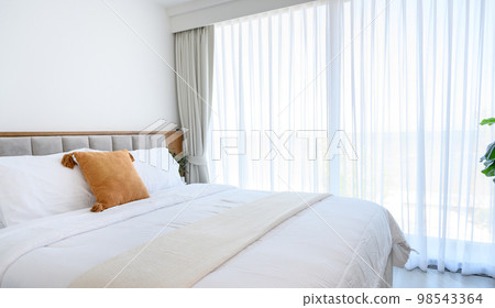 Modern interior cozy bed near a window with white curtains in bedroom. pillows and white soft blanket for rest and sleep. Modern interior cozy bed near a window with white curtains in bedroom. pillows and white soft blanket for rest and sleep. 98543364