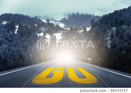 Yellow GO word written on highway road in the middle of empty asphalt road through the pine forest. 98543557