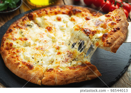 A slice of hot Italian pizza with stretching cheese. Pizza four cheeses with basil. 98544013