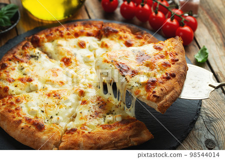 A slice of hot Italian pizza with stretching cheese. Pizza four cheeses with basil. 98544014