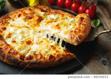 A slice of hot Italian pizza with stretching cheese. Pizza four cheeses with basil. 98544015