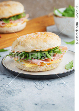 Two homemade sandwiches with ham, cheese and arugula on a concrete table. 98544019
