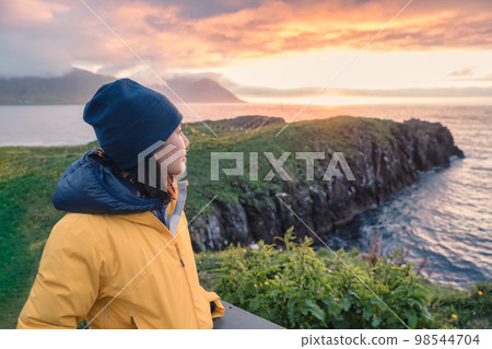 Young asian woman standing and watching puffin bird on the cliff on summer at East of Iceland Young asian woman standing and watching puffin bird on the cliff on summer at East of Iceland 98544704