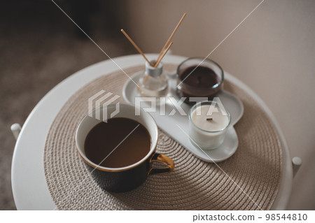 Cup of fresh coffee with scented candles and liquid home fragrance in glass bottle with bamboo sticks on table in room closeup. 98544810