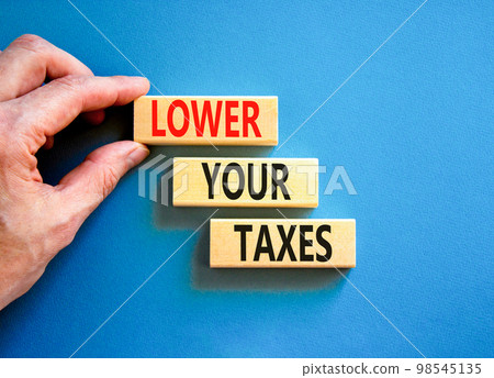 Lower your taxes symbol. Concept words Lower your taxes on wooden blocks on a beautiful blue table blue background. Businessman hand. Business tax lower your taxes concept. Copy space. Lower your taxes symbol. Concept words Lower your taxes on wooden blocks on a beautiful blue table blue background. Businessman hand. Business tax lower your taxes concept. Copy space. 98545135