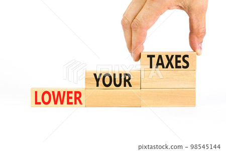 Lower your taxes symbol. Concept words Lower your taxes on wooden blocks on a beautiful white table white background. Businessman hand. Business tax lower your taxes concept. Copy space. 98545144