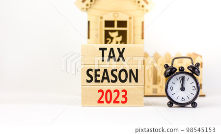 Tax season 2023 symbol. Concept words Tax season 2023 on wooden blocks on a beautiful white table white background. Black alarm clock, house model. Business Tax season 2023 concept. Copy space. 98545153