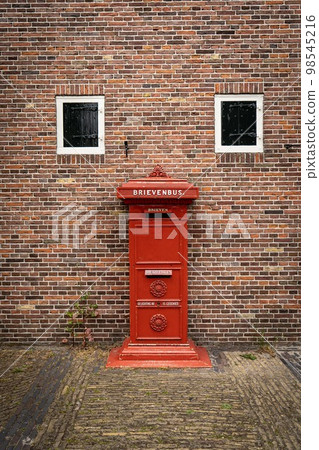 traditional old Dutch red postbox mounted in a cotswold stone wall 98545216