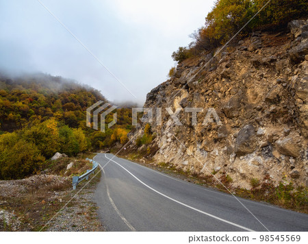 Empty morning highway through the pass in thick fog. Beautiful asphalt freeway, motorway, highway through of caucasian landscape mountains hills at cold weather in mid october. Ingushetia. Empty morning highway through the pass in thick fog. Beautiful asphalt freeway, motorway, highway through of caucasian landscape mountains hills at cold weather in mid october. Ingushetia. 98545569