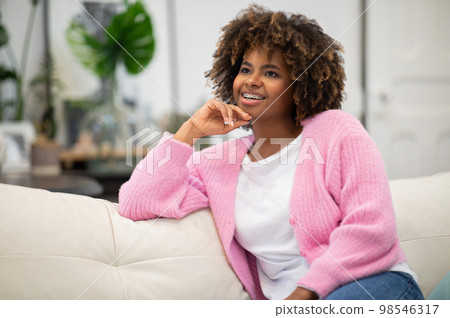 Dreamy cheerful african curly woman resting on couch at home 98546317