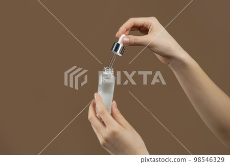 Closeup shot of young lady holding moisturizing serum, using hyaluronic acid, standing on brown background 98546329