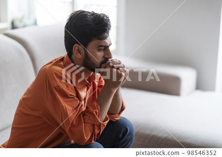 Frustrated arab guy sitting on sofa at home, side view 98546352