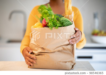 Millennial african american woman in casual unbaking paper bag with organic vegetables Millennial african american woman in casual unbaking paper bag with organic vegetables 98546365