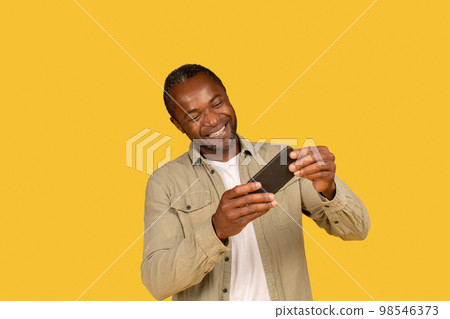 Happy middle aged african american male in casual play online game on phone, enjoy spare time Happy middle aged african american male in casual play online game on phone, enjoy spare time 98546373