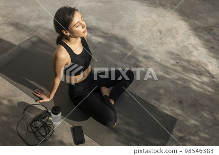 Happy muscular slim young european lady athlete in sportswear sits on mat with bottle of water 98546383