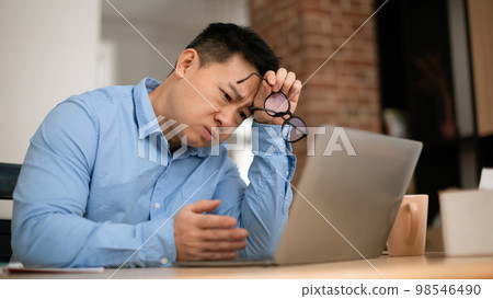Boring tired mature asian businessman working on laptop computer, sitting at table at home office, panorama 98546490