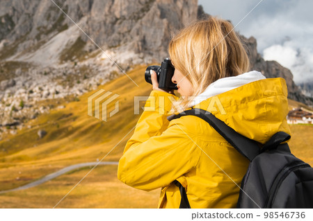 Woman takes photos of scenic Passo Giau pass. Traveler with backpack uses camera to capture Italian Alps Woman takes photos of scenic Passo Giau pass. Traveler with backpack uses camera to capture Italian Alps 98546736