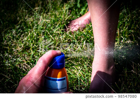 Applying an aerosol spray sunscreen to a young child in the summer.  98547080