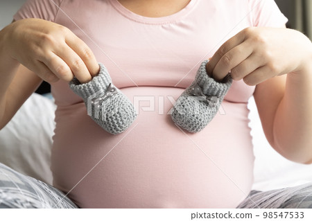 Pregnant woman holds two little wool booties on belly. Healthy pregnancy. Pregnant woman holds two little wool booties on belly. Healthy pregnancy. 98547533