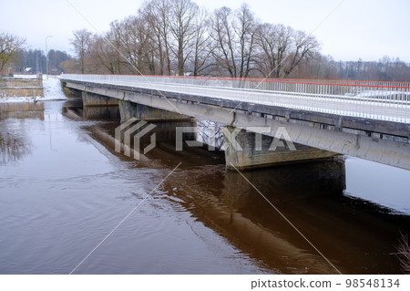 River Aiviekste in Vidzeme, Latvia in winter time. High water level in the river, dark January day. Bridge over the river 98548134