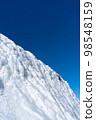 A climber in a red suit climbs an icy white mountain 98548159