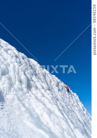 A climber in a red suit climbs an icy white mountain A climber in a red suit climbs an icy white mountain 98548159