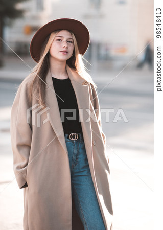 Blonde teen girl 13-14 year old wearing stylish coat and hat walking in city street over autumn nature background close up. Fall season. Teenagerhood. 98548413