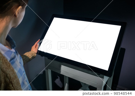 Woman using interactive empty white touchscreen display kiosk at exhibition Woman using interactive empty white touchscreen display kiosk at exhibition 98548544