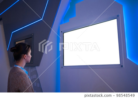 Woman looking at blank white display wall at exhibition - white screen concept 98548549