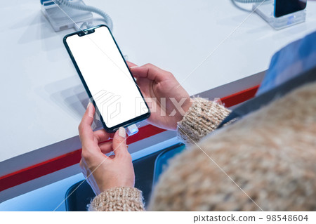 Mock up: woman looking at smartphone with blank white screen at store, shop Mock up: woman looking at smartphone with blank white screen at store, shop 98548604