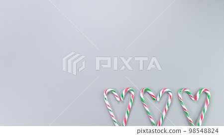 Red, green and white candy canes in the shape of heart on grey background. Valentine's Day concept. Greeting card with copy space for your text or advertising, flat lay. 98548824